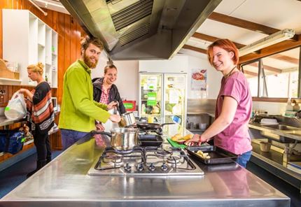YHA Te Anau youth travelers preparing meals in communal kitchen area
